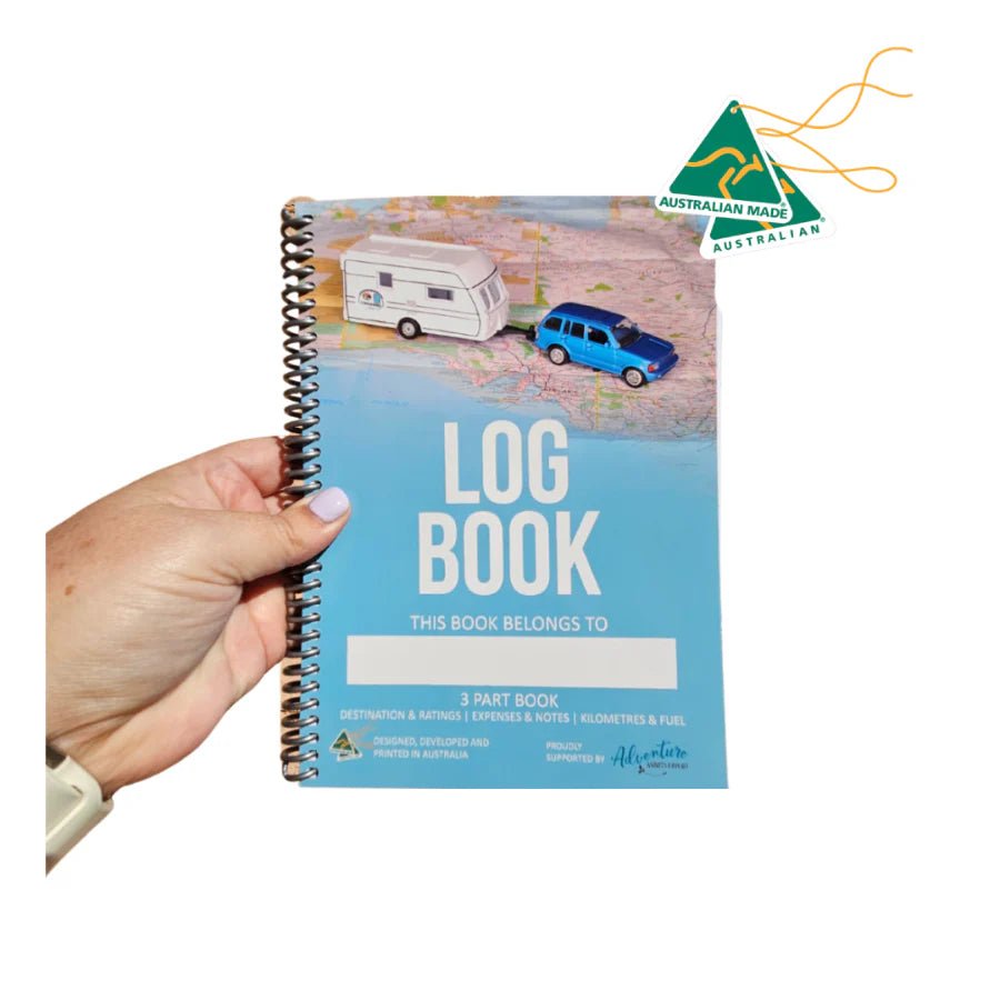 Hand holding the Adventure Awaits Australian-made Caravan and Camper Log Book showing the front cover with caravan and 4WD illustration and 3-part book details