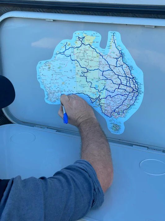 Grey nomad tracing travel routes on an Adventure Awaits Map of Australia UV outdoor sticker decal stuck to the outside of a caravan storage door using a marker pen