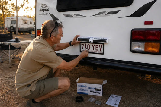 Man installing a wireless reverse camera on a Jayco caravan number plate bracket at a campsite