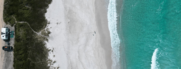 Aerial view of caravan and 4WD camping beside a white sand beach in Australia