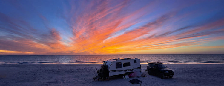 4WD and caravan camping on a remote Australian beach at sunset with vibrant orange and pink skies